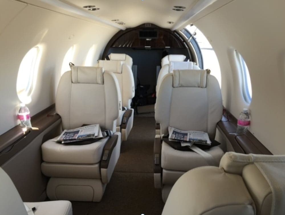 The interior of the aircraft features white leather seats and a dark wood trim.