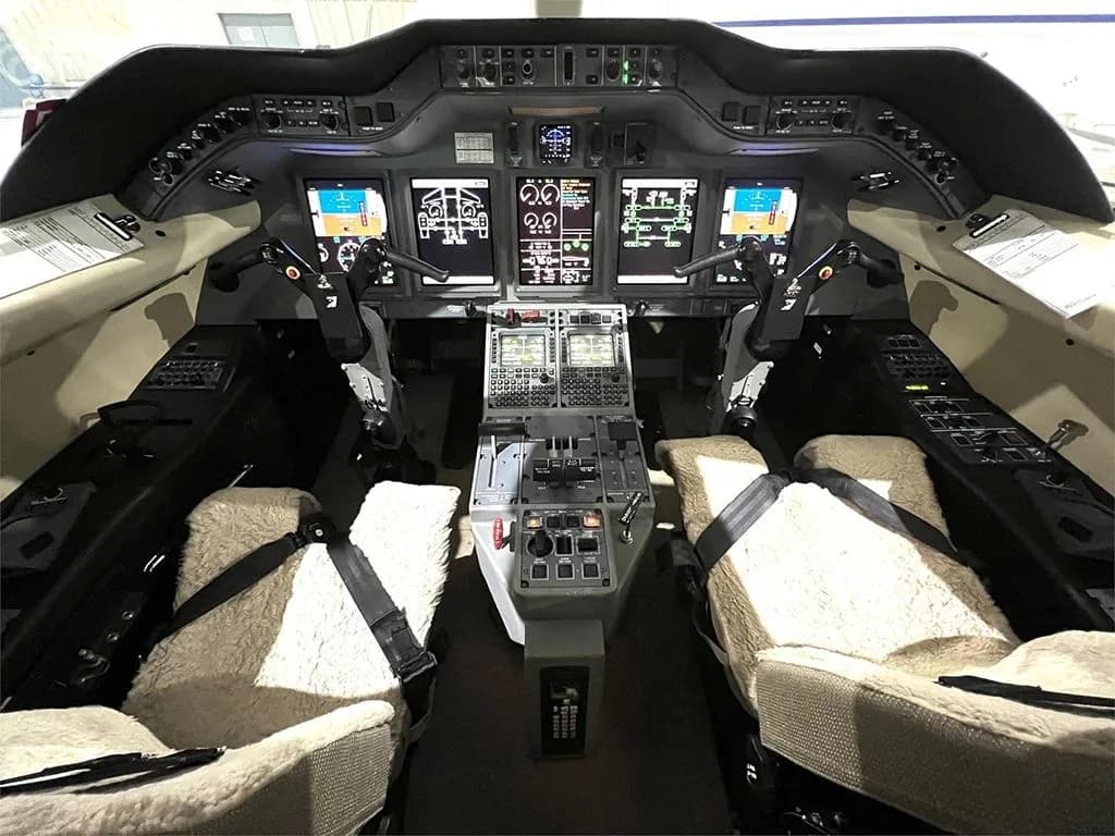 The cockpit of a business jet features multiple digital displays, control yokes, and sheepskin-covered pilot seats.