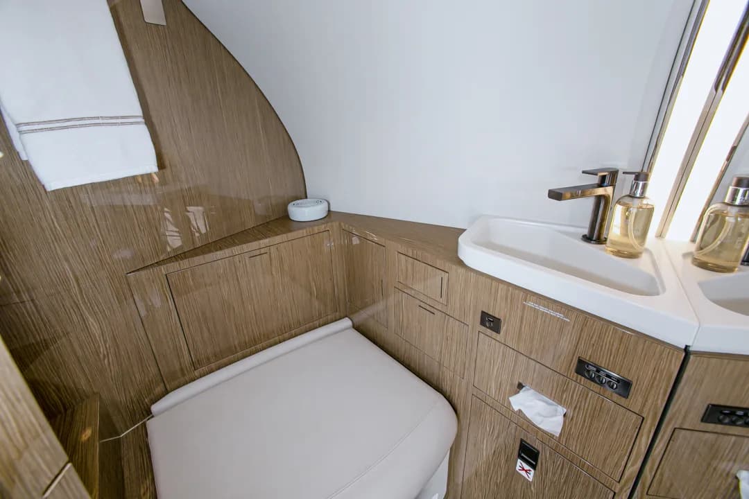 A compact aircraft lavatory with a white toilet, sink, and wooden cabinetry.