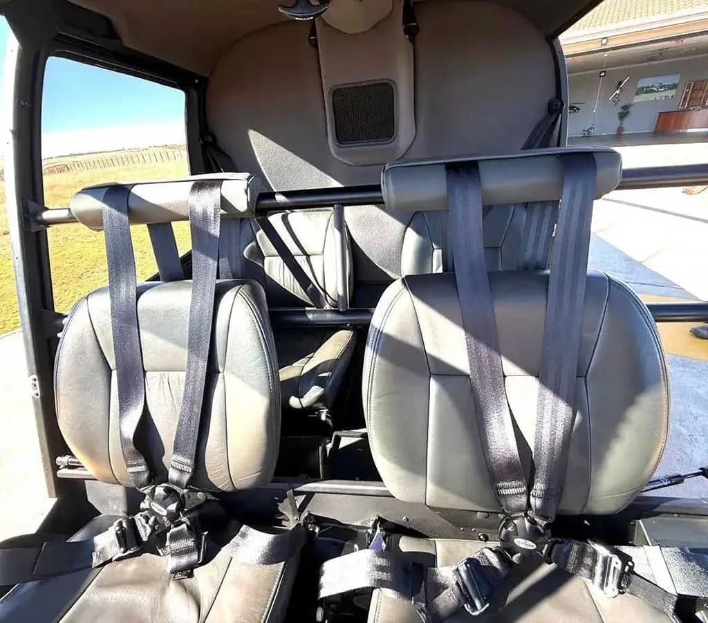 The grey leather passenger seats with black harnesses inside a helicopter cabin.