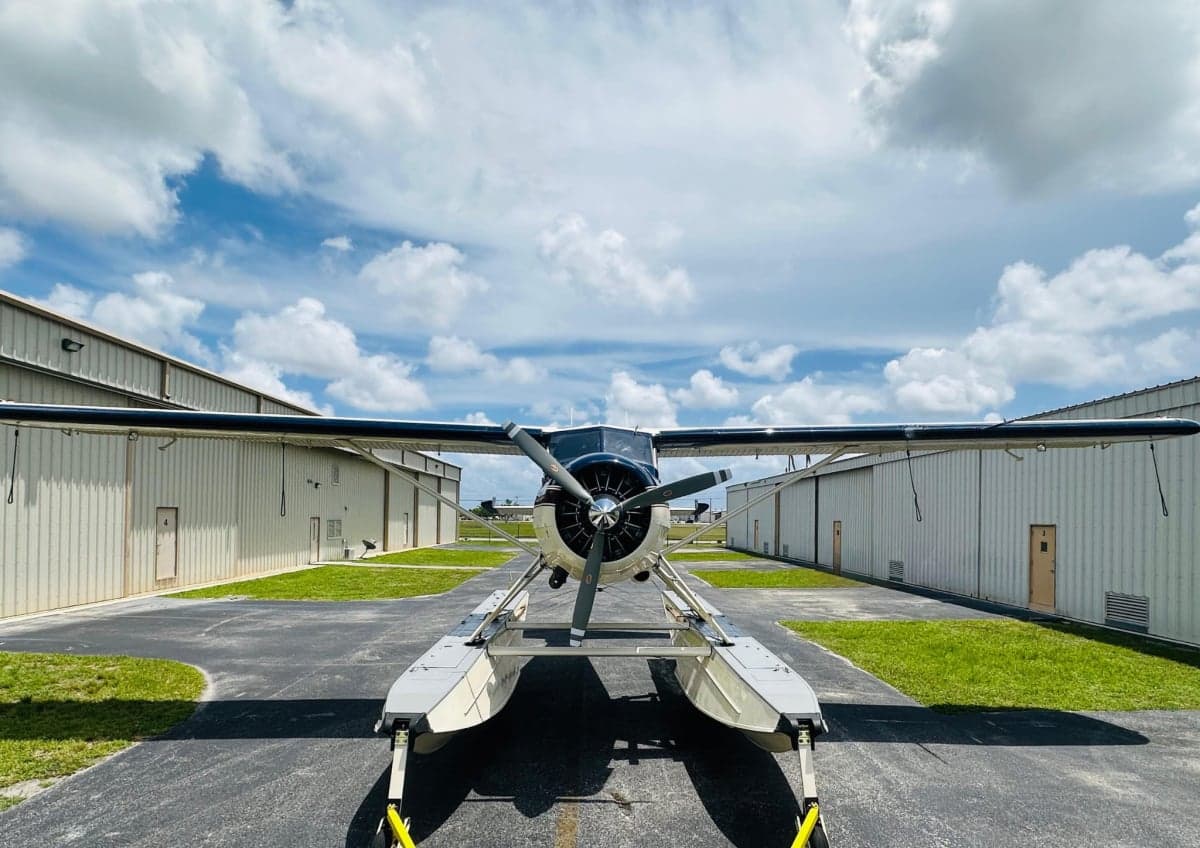 Front view of a white and maroon floatplane on the tarmac.