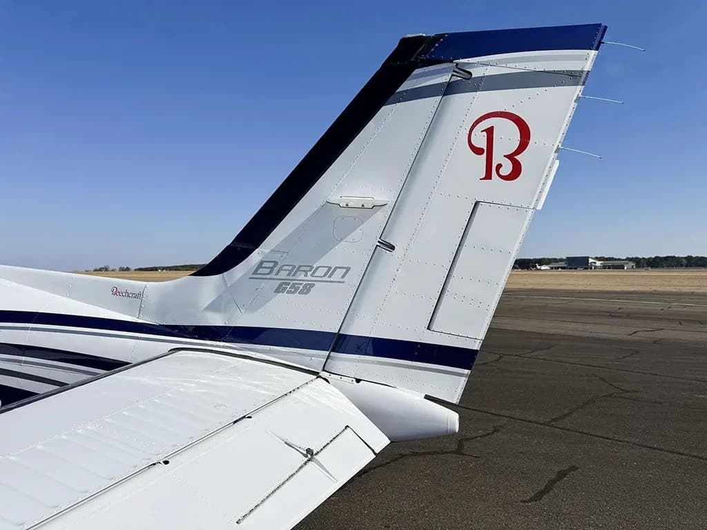 A close-up view of the tail of a white and blue Beechcraft Baron G58, showing the "B" logo.