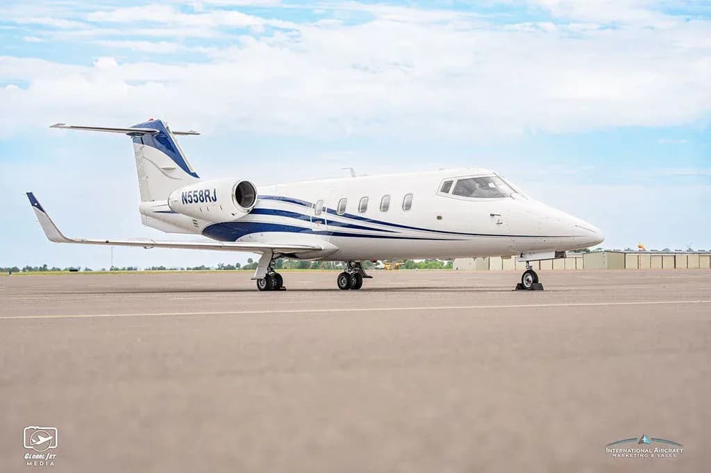A side view of a white business jet with blue stripes, tail number N558RJ, parked on an airfield.