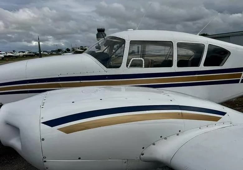 A close-up view of the white fuselage and wing of a twin-engine aircraft with blue and gold stripes, parked at an airport.