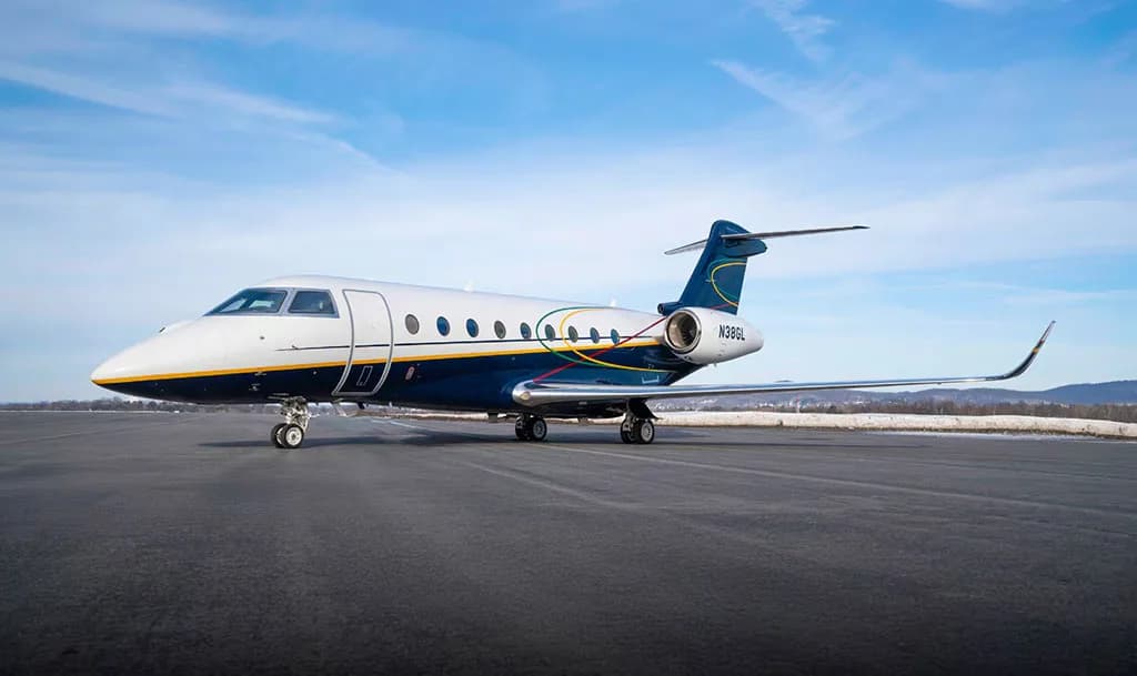 A Gulfstream G550 aircraft, registration N38GL, with a white and dark blue livery, is seen from a side view on a winter airfield.