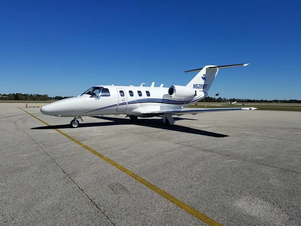 A white Cessna Citation CJ3 with blue stripes sits on the tarmac.
