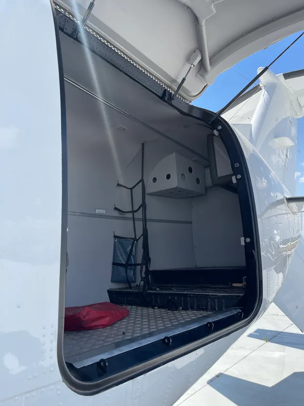 An open cargo door revealing a spacious, empty compartment with a red bag inside a white aircraft.