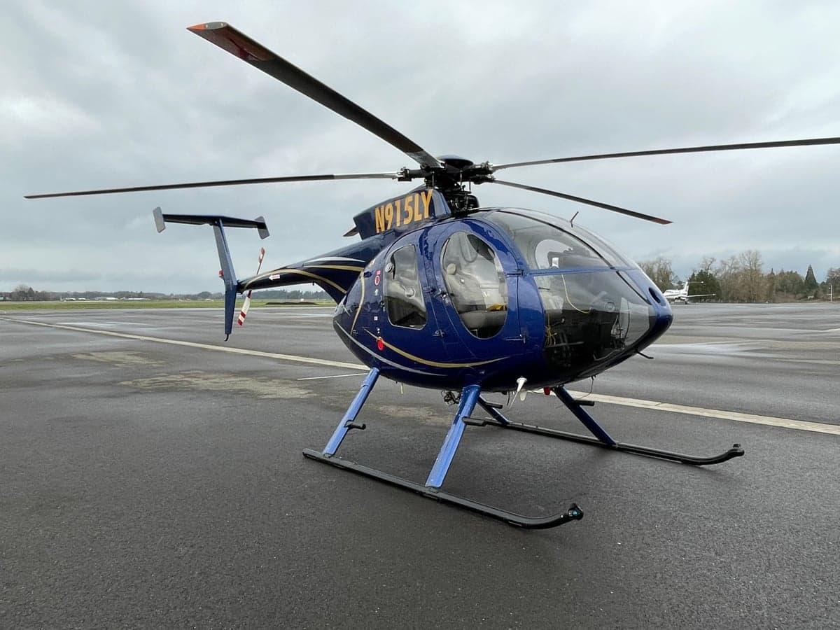 A blue MD 500 helicopter is parked on an airport tarmac.