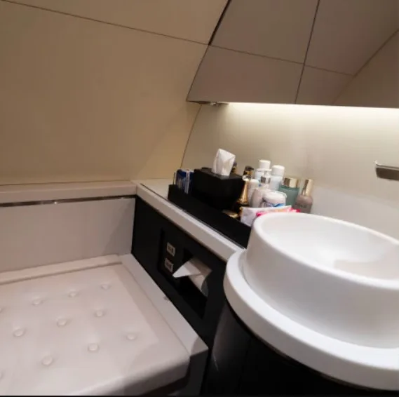 A modern aircraft lavatory with a white sink, toiletries, and a padded bench seat.