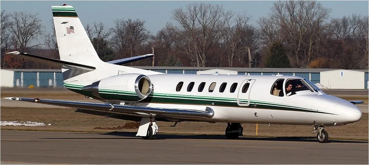 A white business jet with a green stripe on its fuselage and tail, taxiing on an airfield.