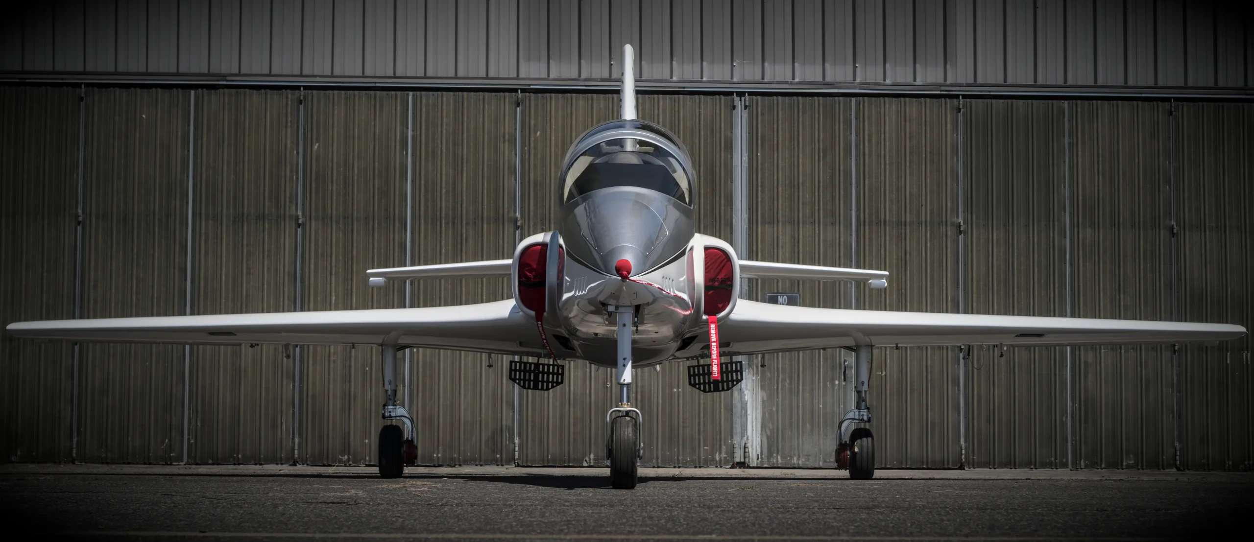 A white and silver Viperjet aircraft with red accents, viewed head-on in front of a hangar.