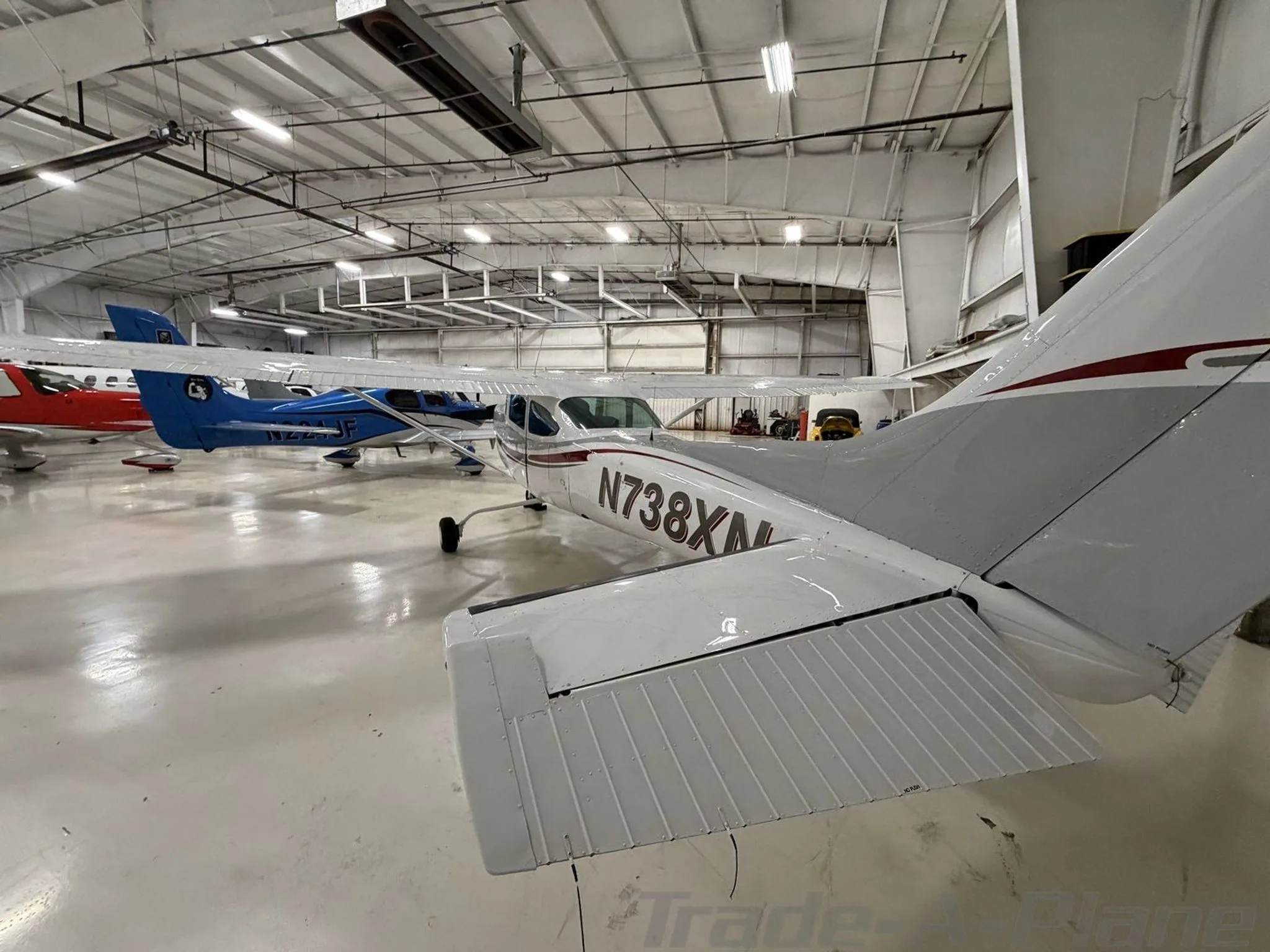 A rear quarter view of a white and grey Cessna 182 with N738XN registration in a hangar.