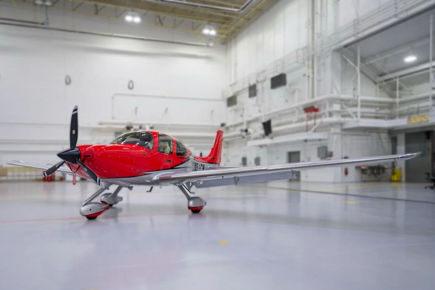 A three-quarter front view of a red and white Cirrus SR22 aircraft with registration N51CW in a hangar.