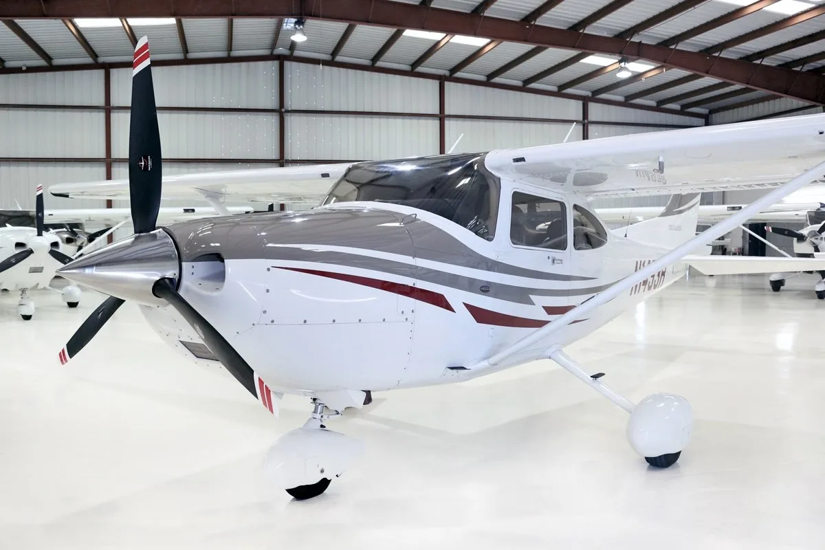 A front-right view of the white Cessna Skylane N1493R with grey and maroon stripes, parked in a hangar.