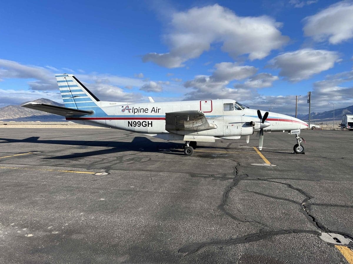 A Beechcraft King Air with a white and blue paint scheme is parked on a cracked tarmac.
