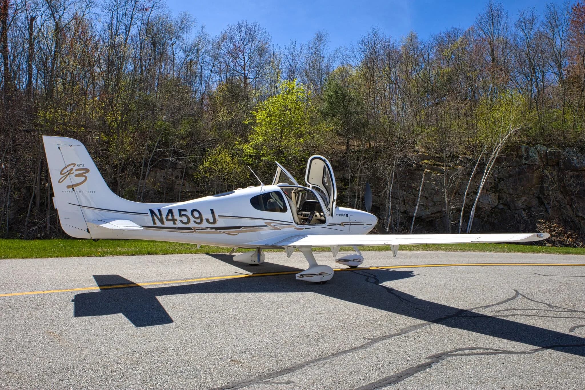 A side view of the white Cirrus SR22 GTS Generation Three aircraft (N459J) with both gull-wing doors open, parked on an airfield.