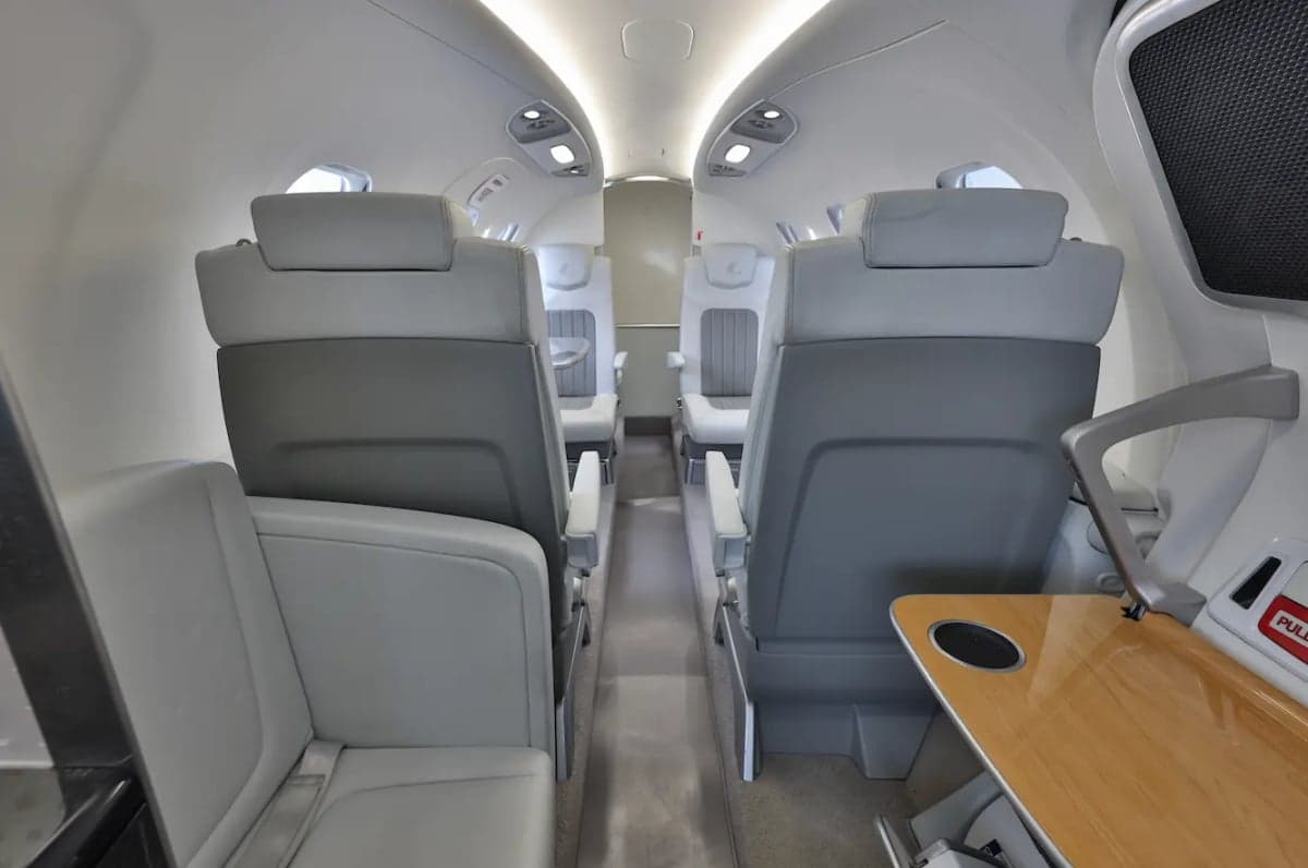 View of the HondaJet HA-420 cabin looking aft, showing rows of light gray and white seats and a side table.