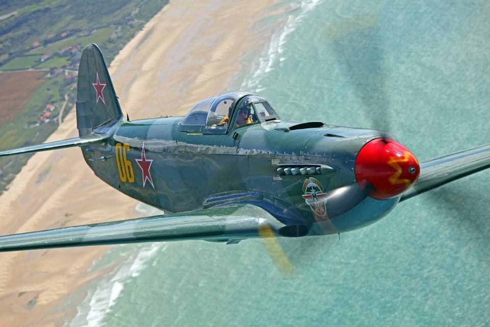 Yak-3 and F4U Corsair in flight over farmland.