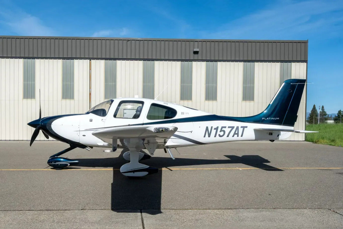 A side view of a white and dark blue Cirrus SR22 aircraft, registration N157AT, parked on an asphalt apron.