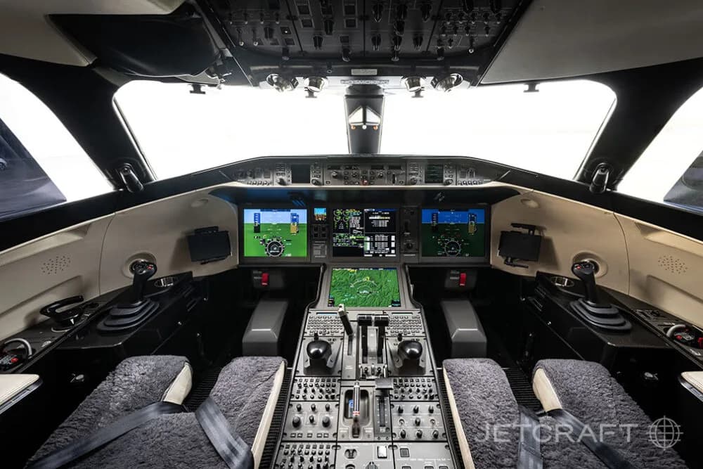 The modern cockpit of a business jet, featuring multiple digital displays and two pilot seats with sheepskin covers.