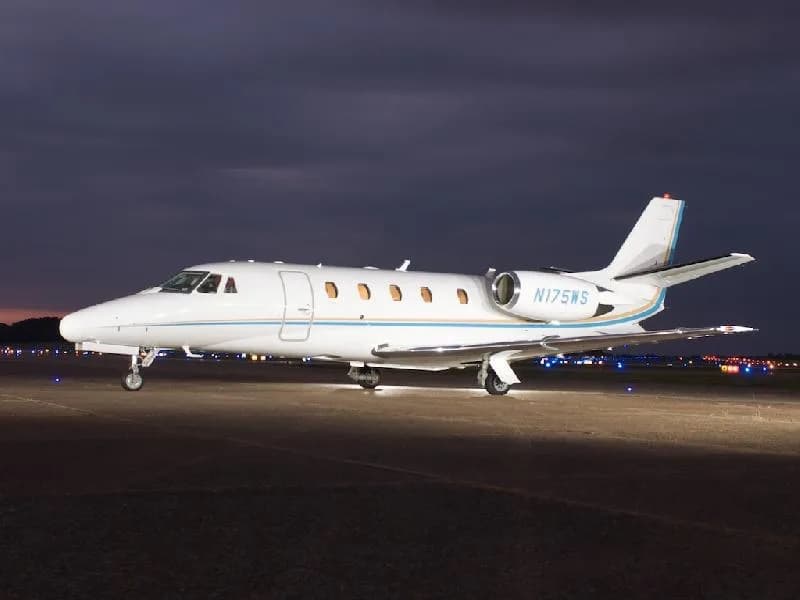 A white jet with blue and gold accents parked on the tarmac at night.