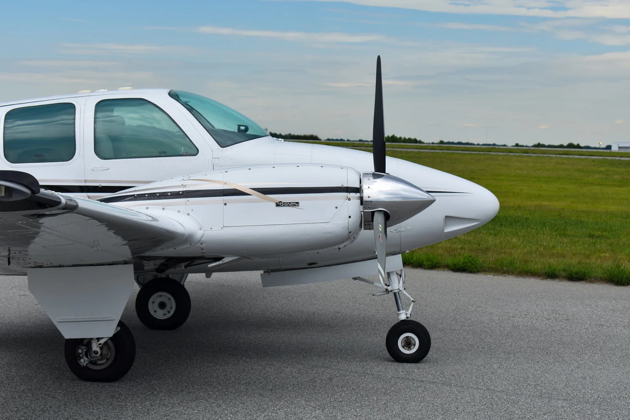 A close-up view of the right engine and nose of a white Beechcraft Baron aircraft on an airfield.
