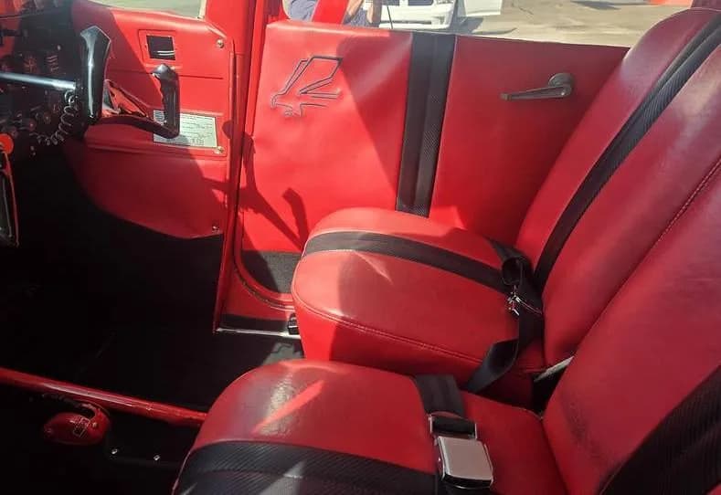 The red interior of an aircraft cabin, showing two seats with black accents and a door panel with an emblem.