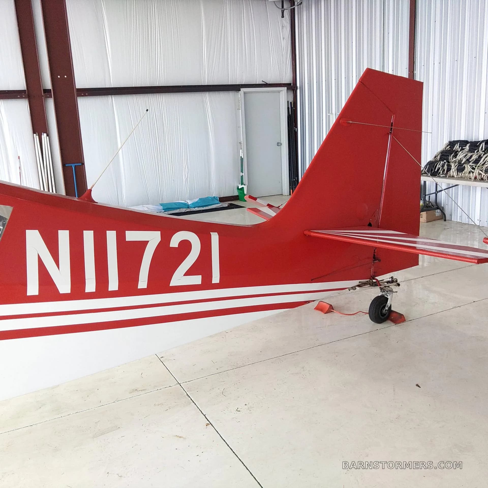 A rear view of the red and white Citabria N11721 aircraft, showing the tail and registration number, inside a hangar.