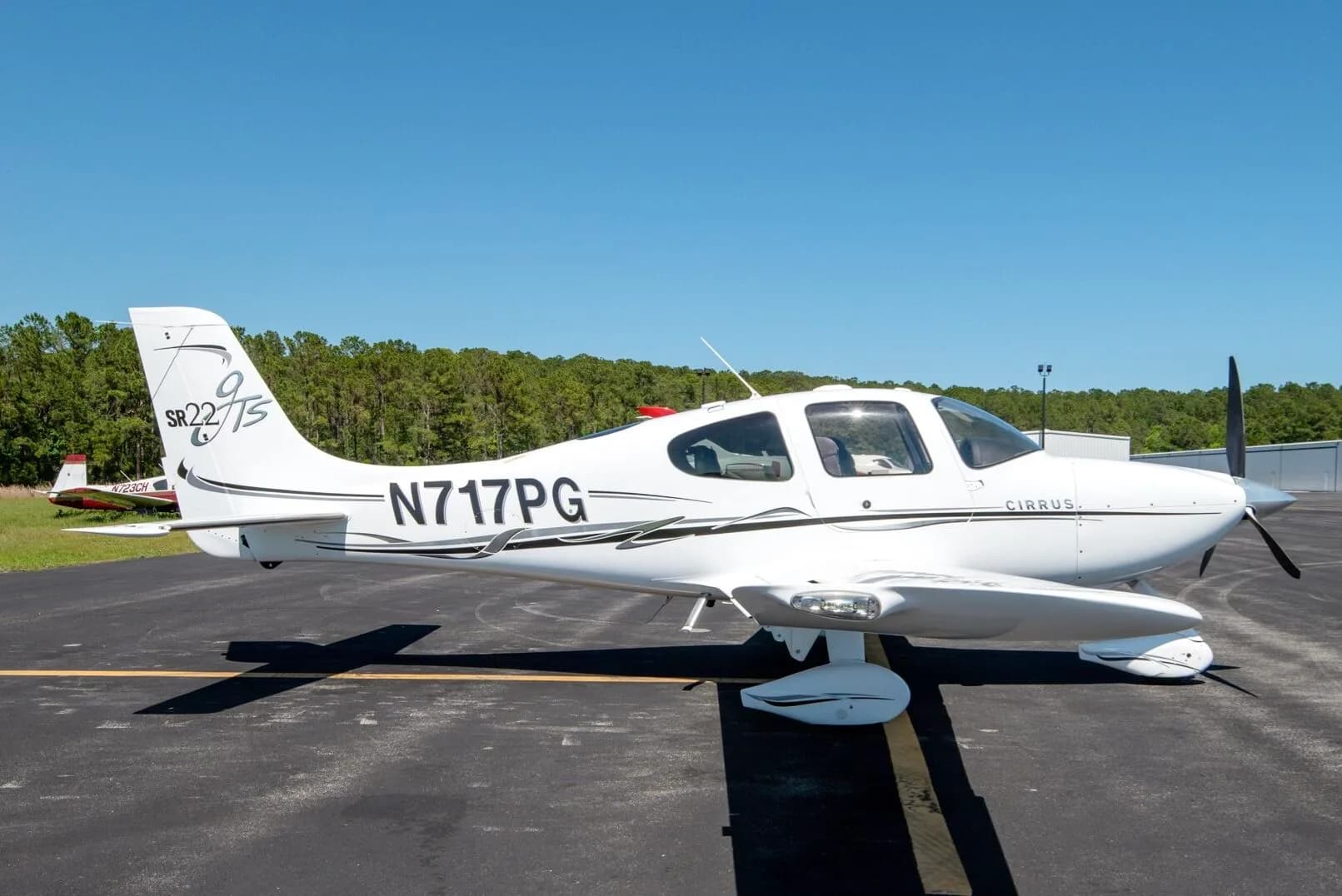 Side view of a white Cirrus SR22T aircraft N717PG with black and grey stripes parked on an airfield.
