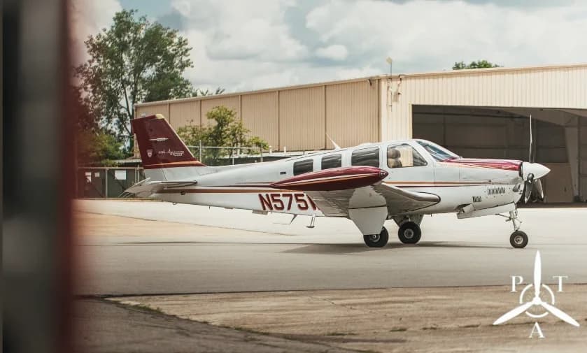 A white and red Beechcraft Bonanza aircraft, tail number N575W, parked on an airfield next to a hangar.