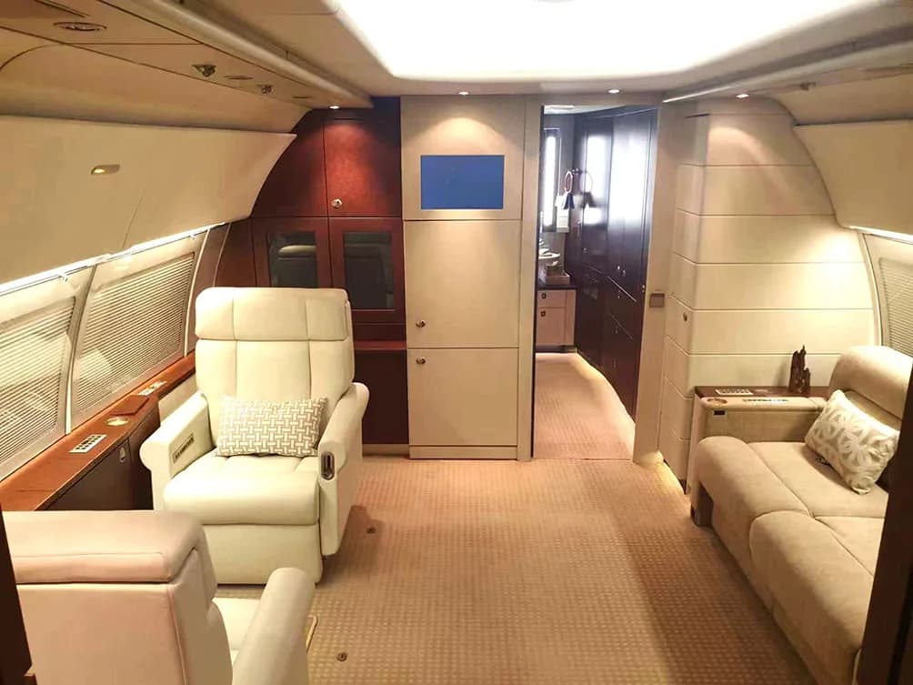 A private jet cabin with a beige armchair and sofa, leading to a galley or private room at the rear.