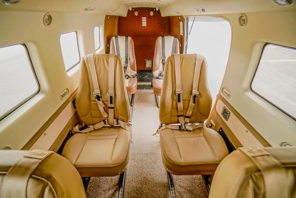 The aircraft interior cabin with tan seats and shoulder harnesses, looking towards the open rear door.