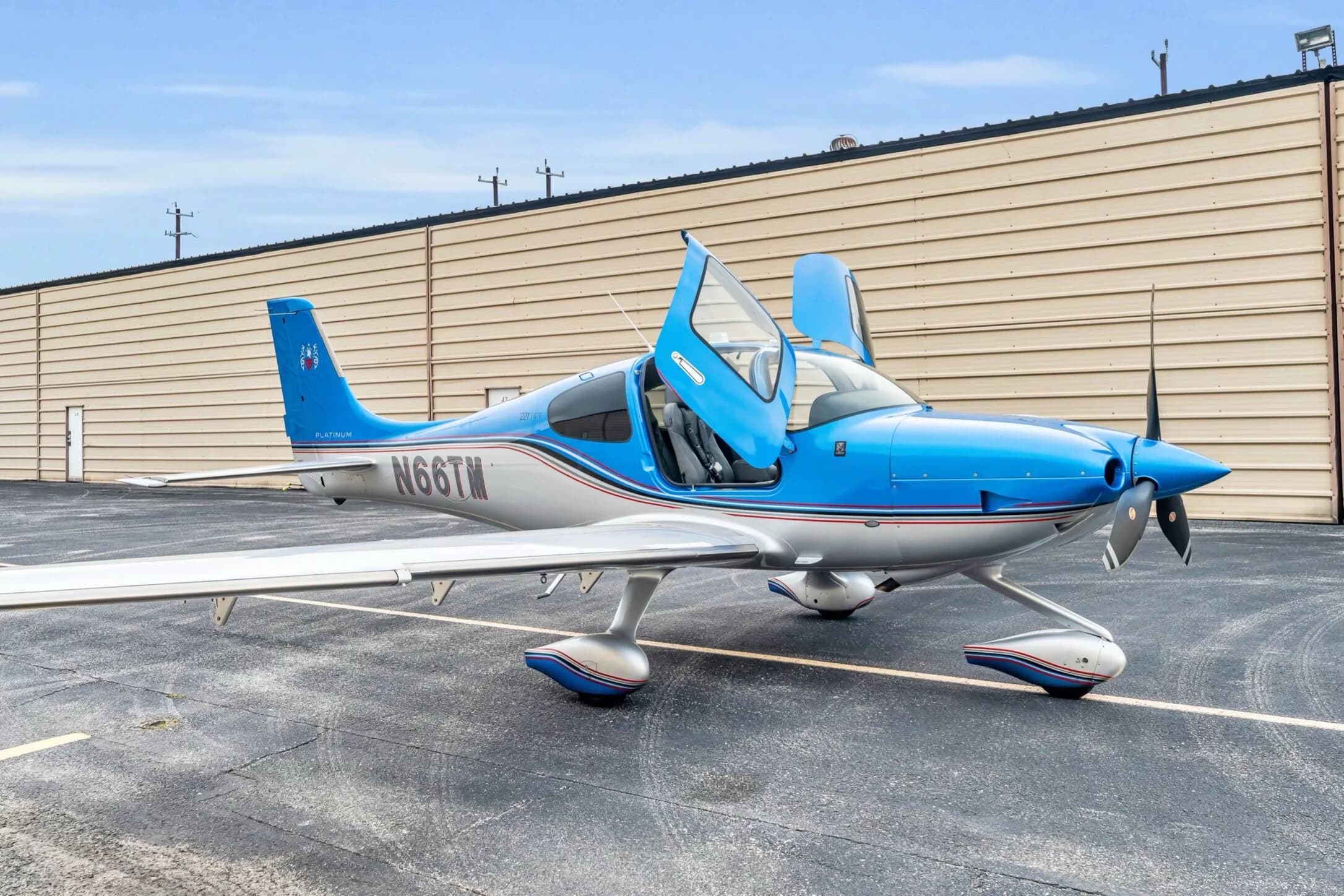 A three-quarter front view of the blue and silver Cirrus SR22T GTS aircraft N66TM with its gull-wing doors open.