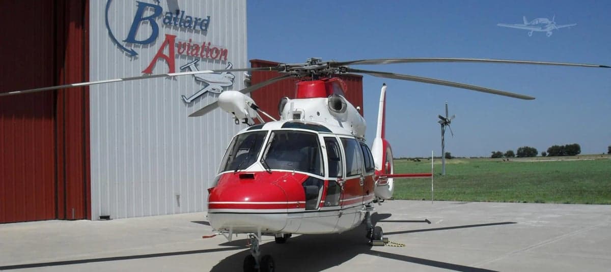 Front view of a red and white helicopter on a tarmac in front of a hangar.