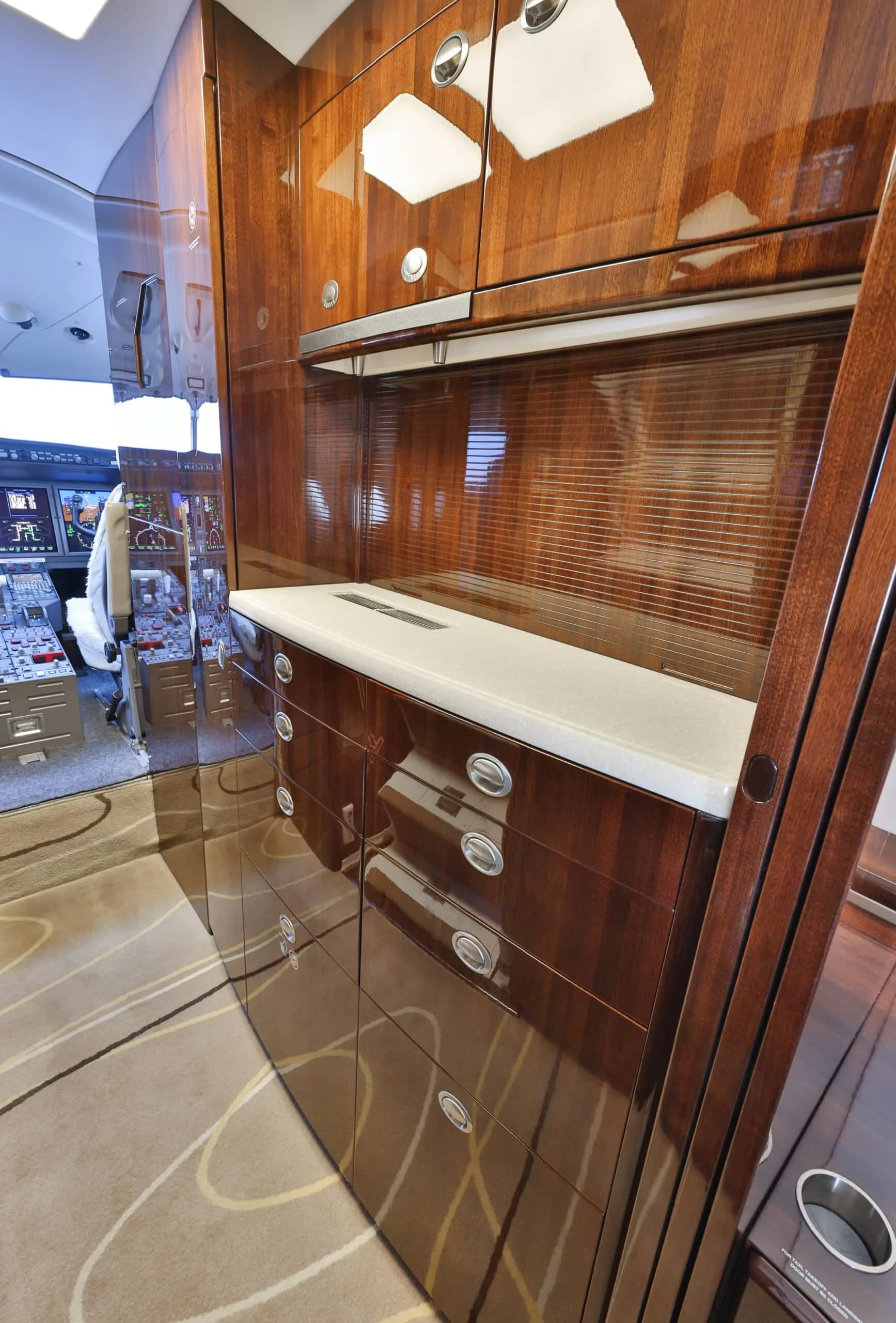 Dark wood cabinetry with a light countertop and drawers is visible in the galley area of a private jet.