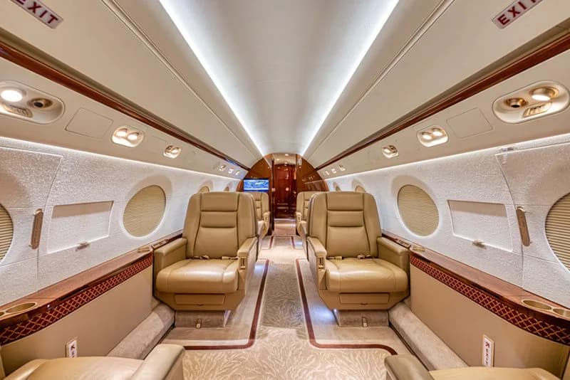 The spacious cabin interior of a business jet with tan leather seats arranged in pairs facing each other.