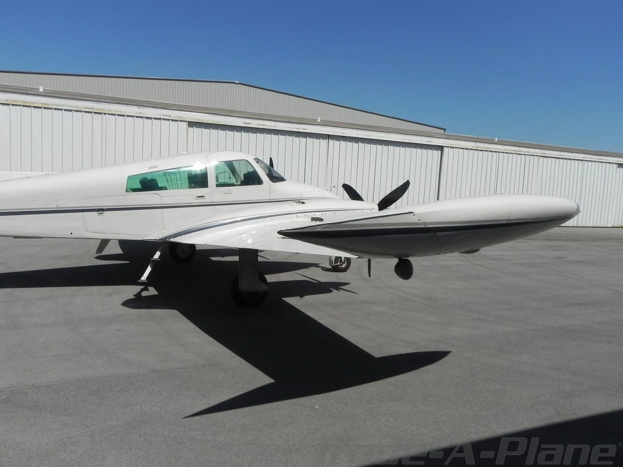 A side view of the fuselage and wing of a white twin-engine Cessna 310 aircraft parked next to a hangar.