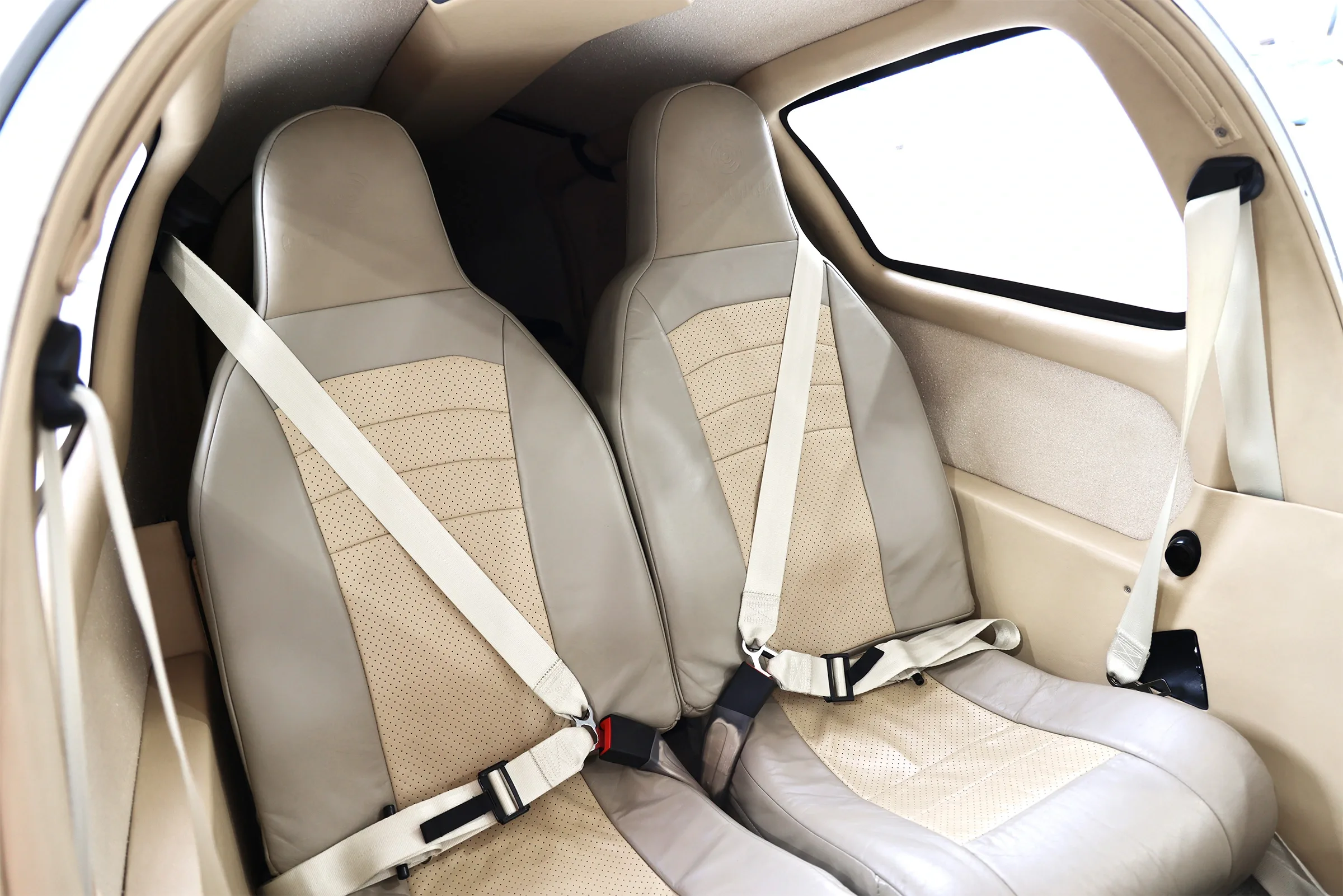 The tan leather interior of an aircraft cabin, showing two front seats with seatbelts.