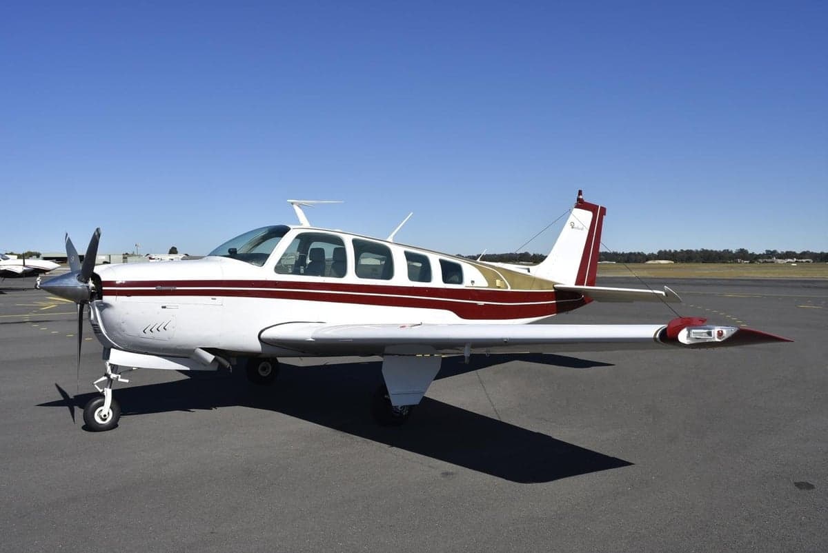 Side view of a white and maroon single-engine aircraft parked on an airfield.