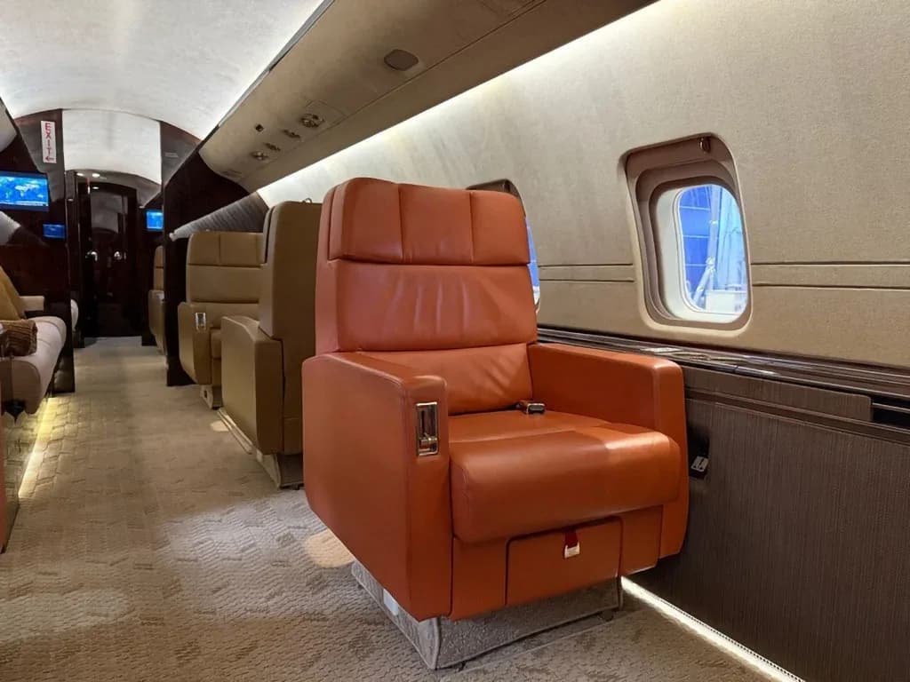 A close-up view of an orange leather seat in the private jet cabin, with a window showing a blue reflection outside.