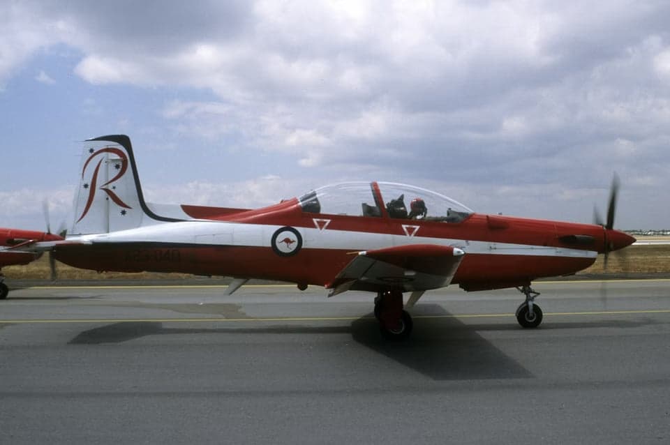 Side view of a red and white Pilatus PC-9 aircraft on the tarmac.