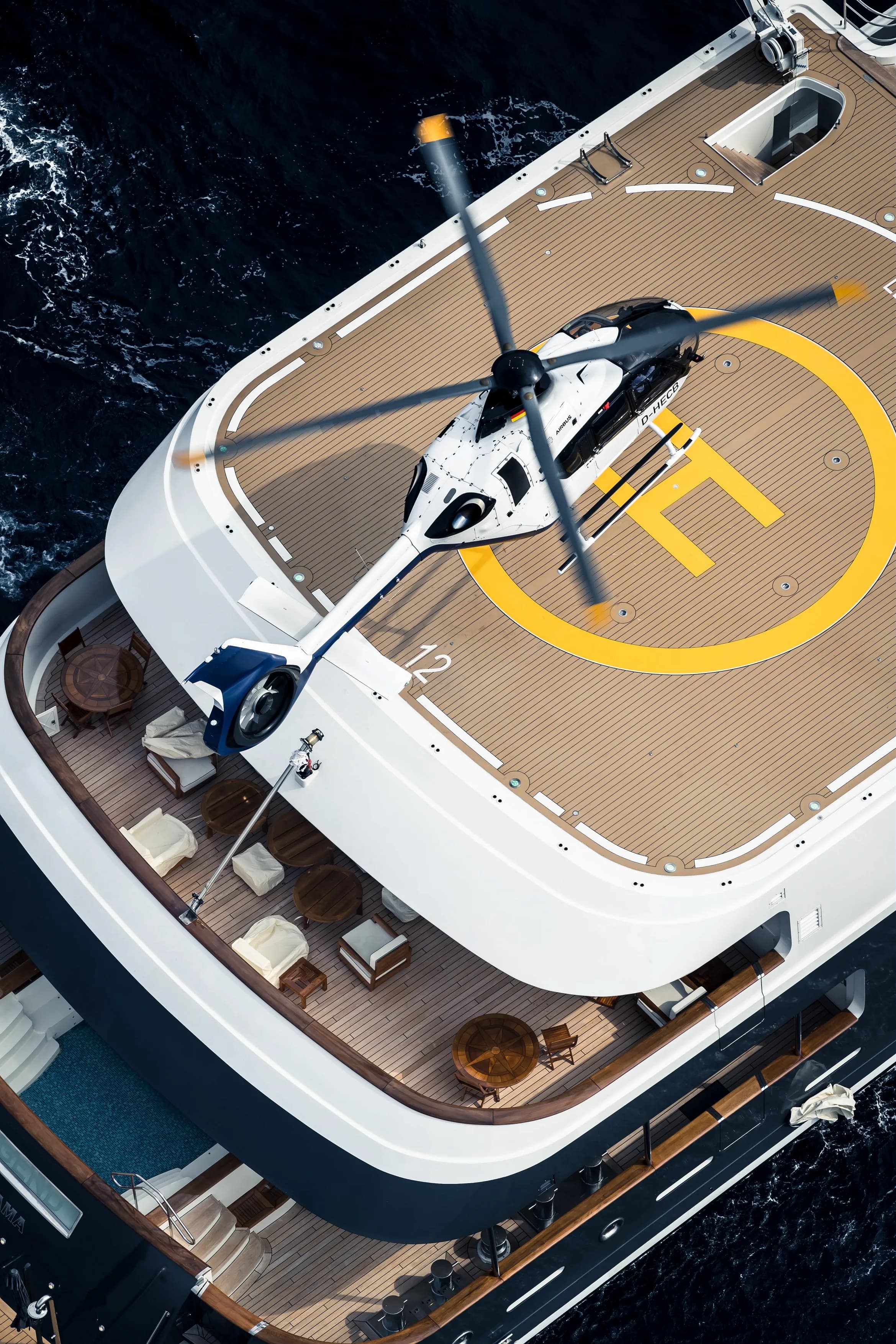 A white and blue Airbus EC135 helicopter landing on a yacht's helipad.