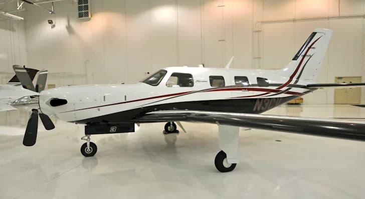 A white and black Piper Meridian aircraft with red accents, registration N3CV, parked in a brightly lit hangar.