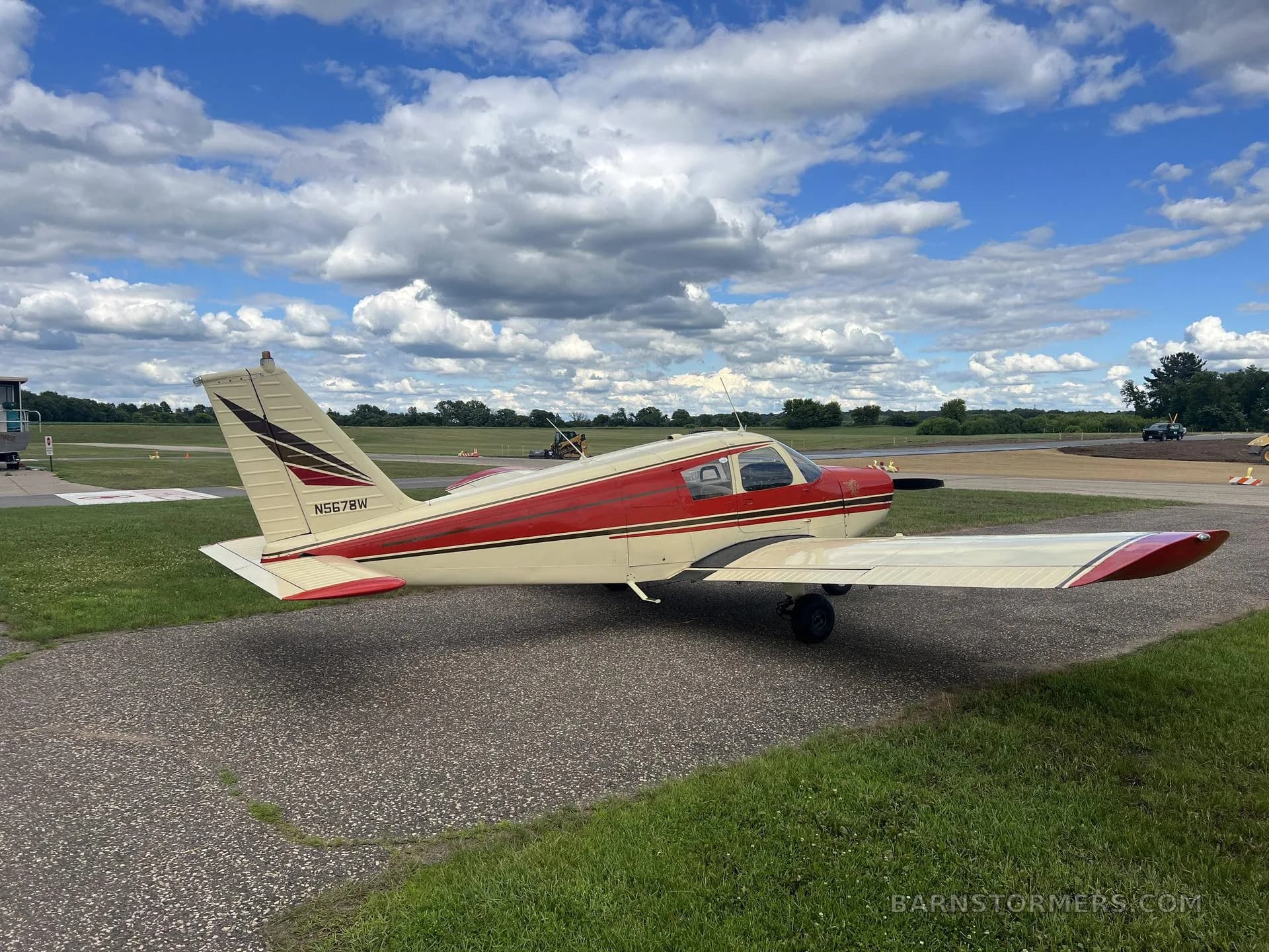 A red and cream single-engine propeller aircraft (N5678W) parked on an airfield ramp under a cloudy sky.