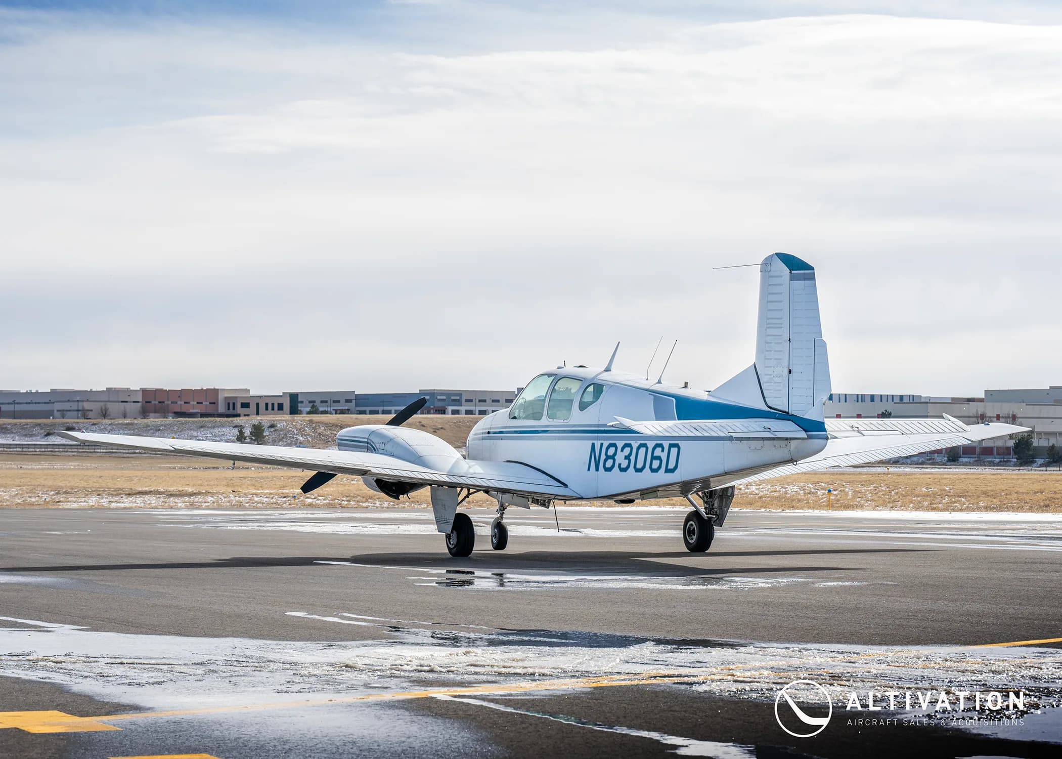 A white and blue twin-engine aircraft with registration N8306D is parked on a tarmac, viewed from the side.