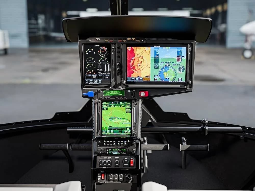 The cockpit of a helicopter features multiple Garmin display screens showing flight and navigation data.