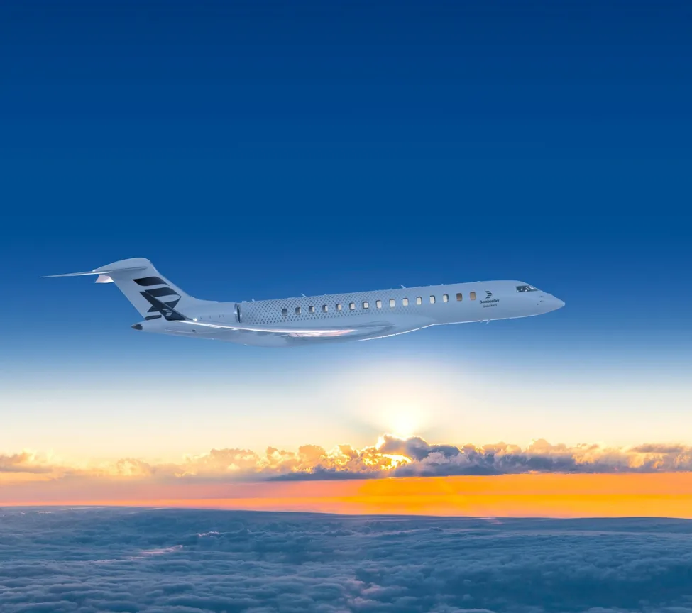 A Bombardier aircraft flying above the clouds at sunset.