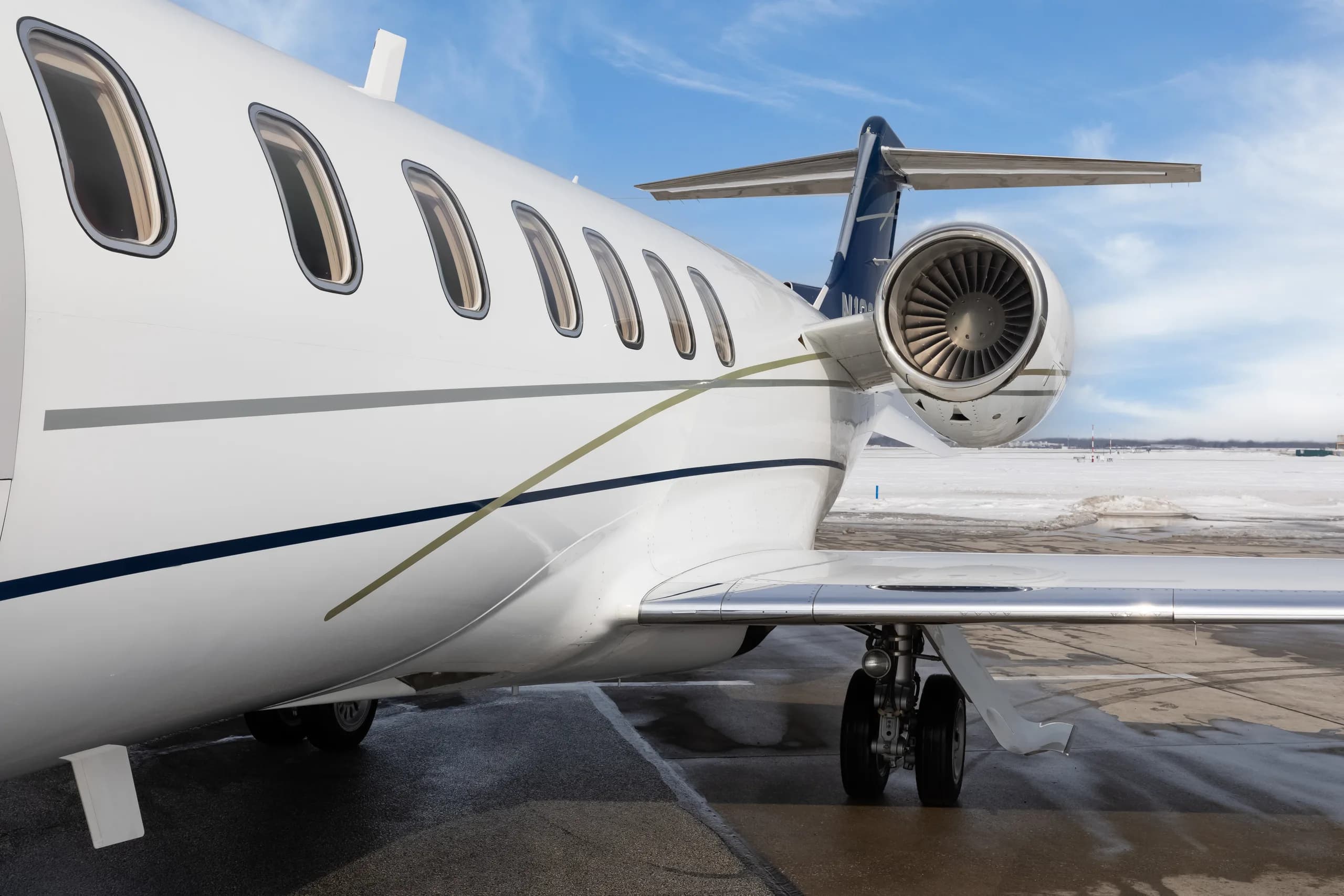 A close-up view of the rear fuselage, engine, and wing of a white Learjet 60 with blue and grey stripes.