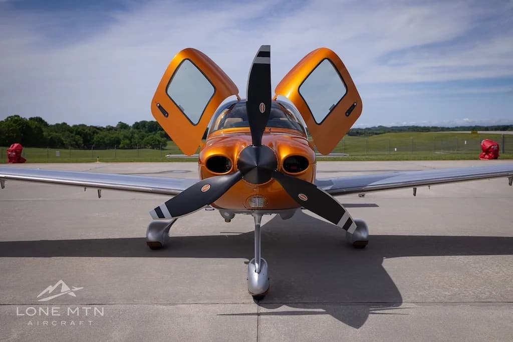 A head-on view of the orange and silver Cirrus SR22T N25BX with its doors open on an airfield.