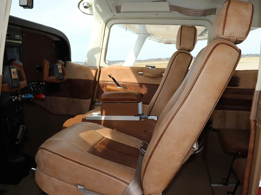 The tan leather interior of an aircraft cabin, showing the front and rear passenger seats.